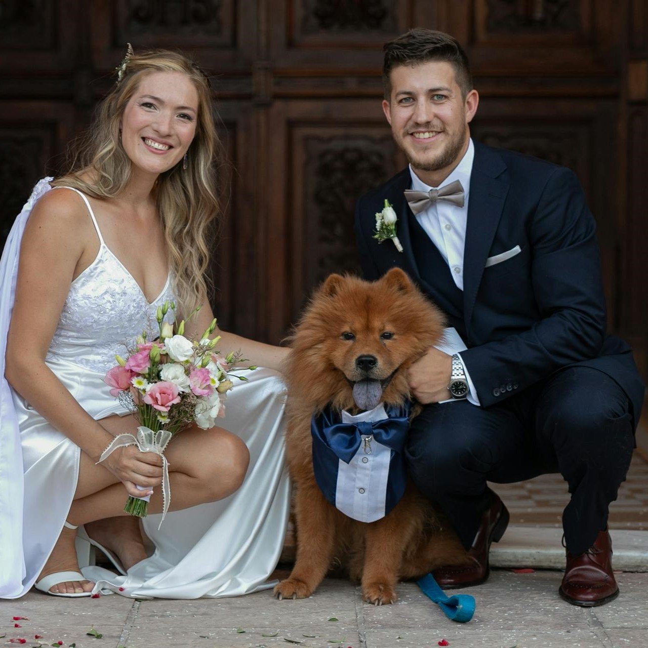 A happy bride and groom on their wedding day, posing for a portrait with their beloved dog.